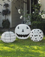 Three decorative pumpkins with black patterns on a grassy lawn.
